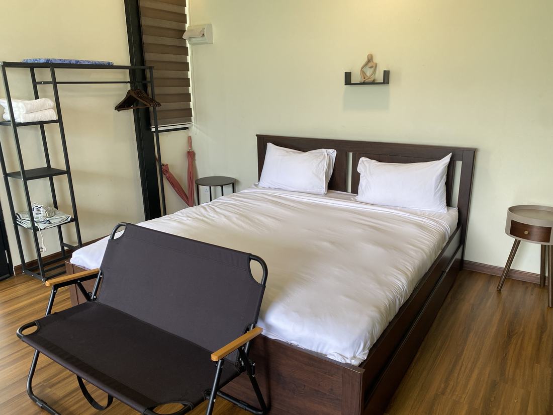 The king bed made up with white linen, a side table and a clothes rack alongside