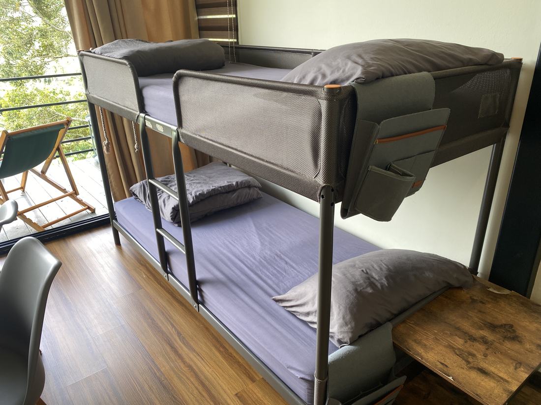 A double-deck bunk made up with pillows and a folded blanket, with a bedside pocket organiser